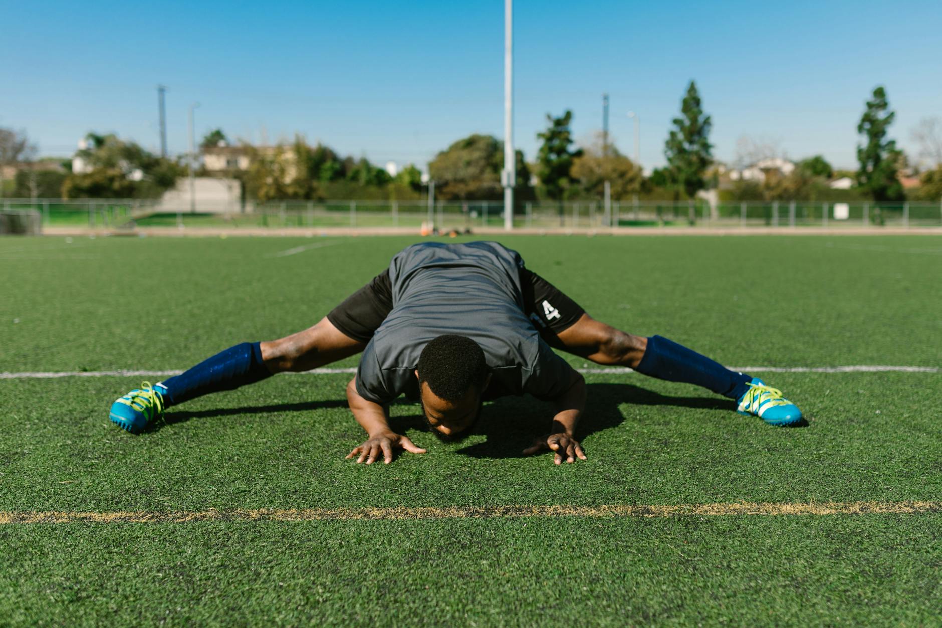 Atleta realizando exercício de alongamento de pernas em pista esportiva ao ar livre
