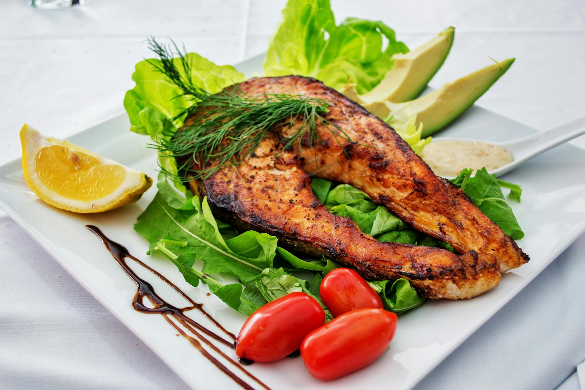 Prato de salmão grelhado servido com abacate, vegetais e folhas verdes sobre uma superfície clara