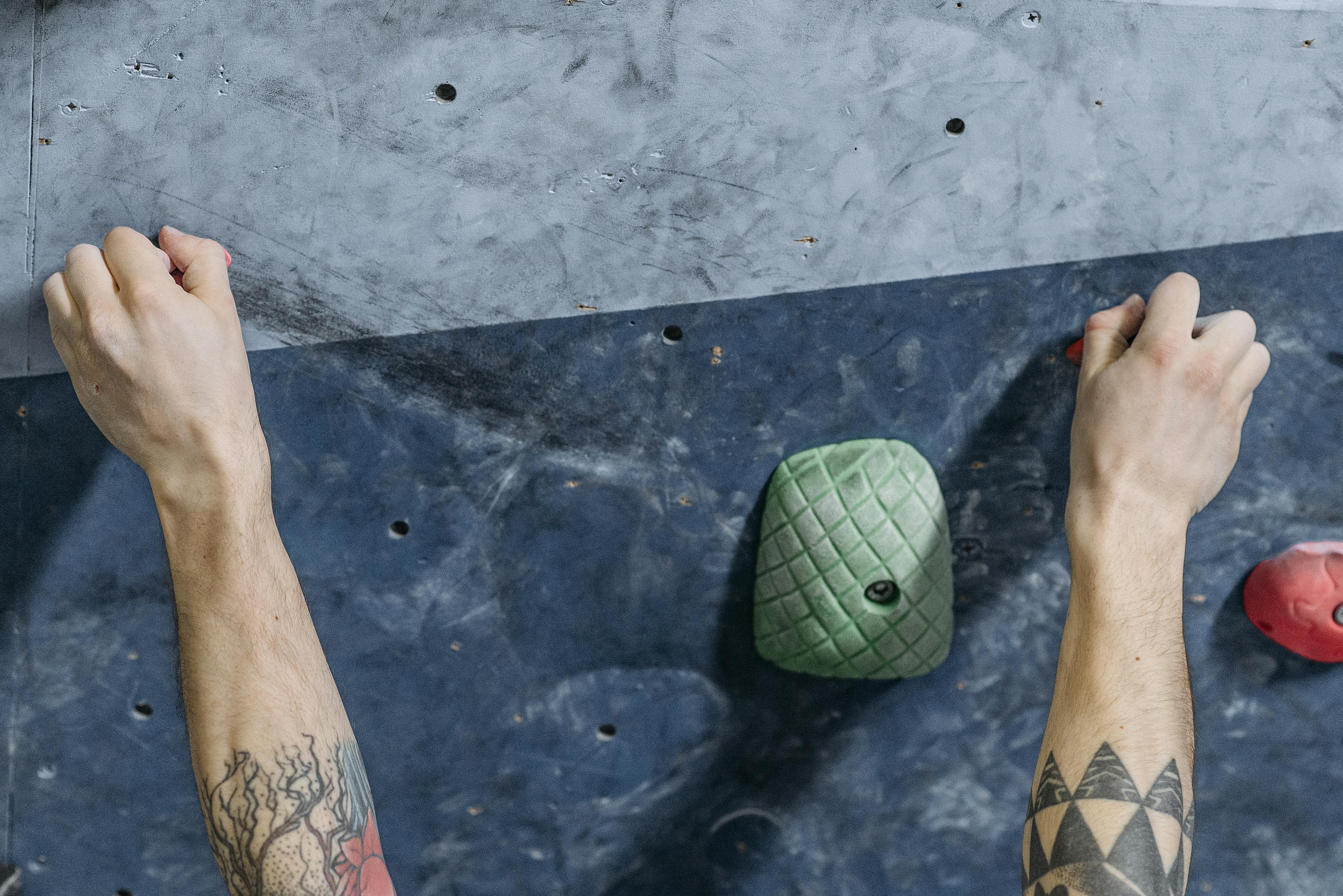 Maos de escalador agarrando firmemente uma agarra colorida em uma parede de escalada indoor, ilustrando a forca de preensao em acao